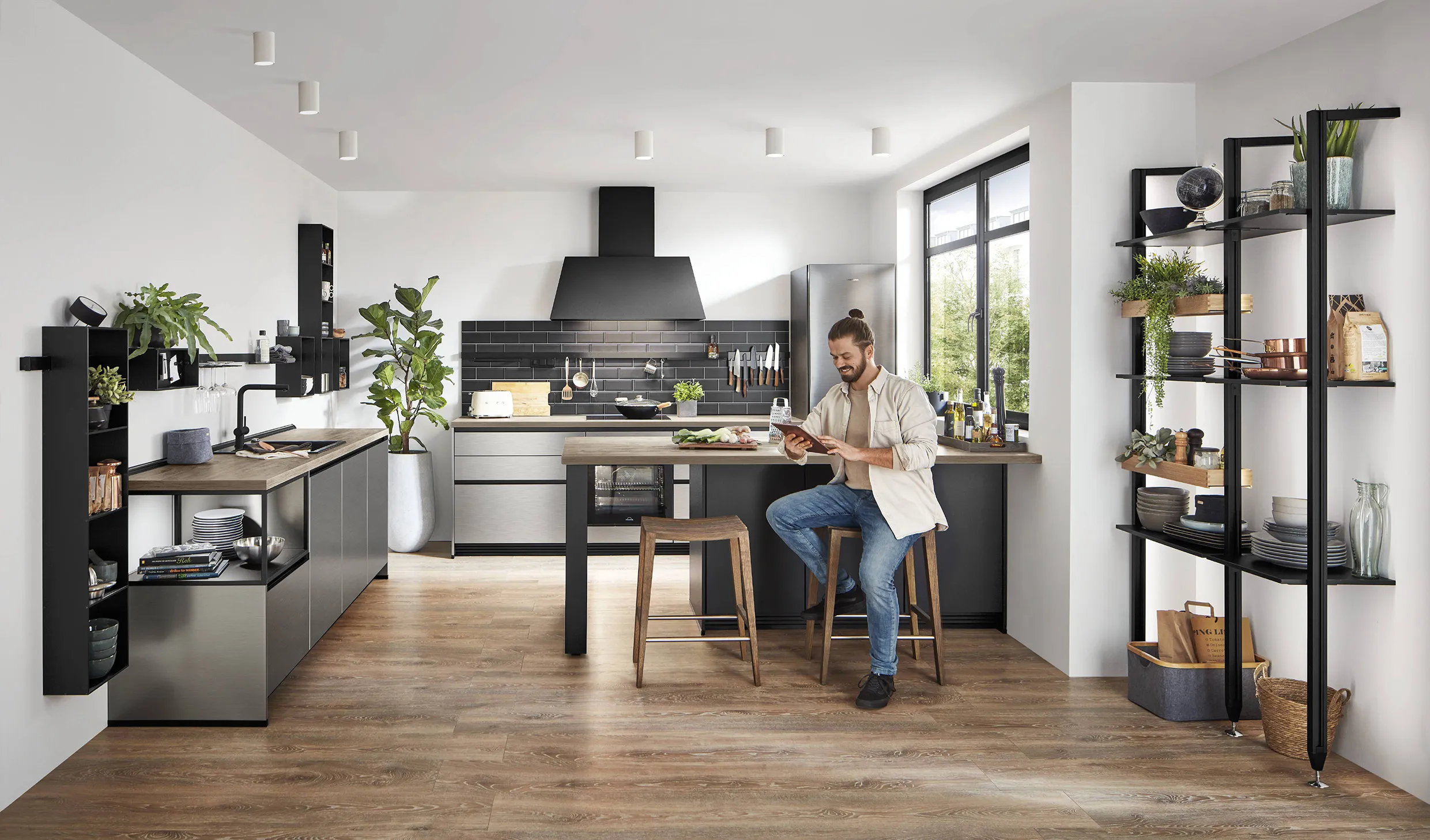 Man sitting at a wooden kitchen island using a smartphone, surrounded by a modern kitchen with smart appliances and sleek shelving. Man sitting at a wooden kitchen island using a smartphone, surrounded by a modern kitchen with smart appliances and sleek shelving.