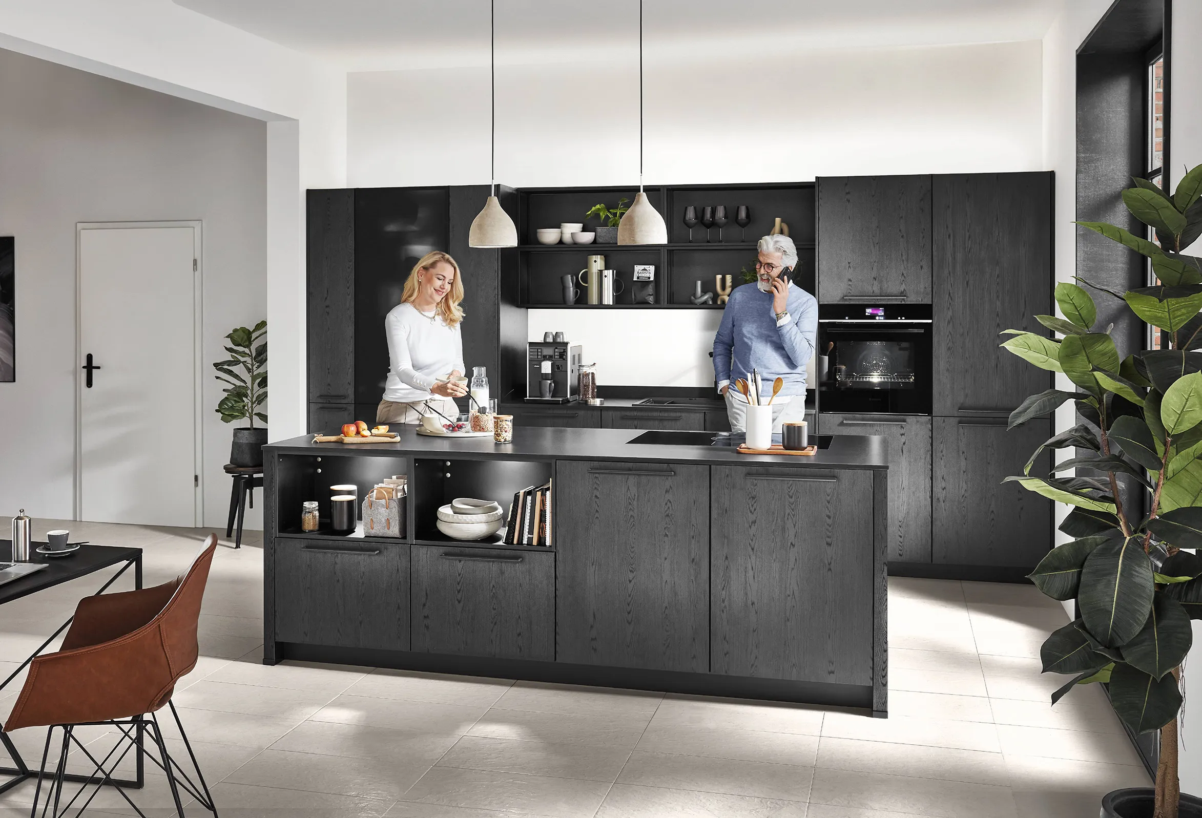 Modern high-ceiling kitchen featuring dark wood cabinets, a large central island with open shelving, and a couple preparing breakfast. Modern high-ceiling kitchen featuring dark wood cabinets, a large central island with open shelving, and a couple preparing breakfast.