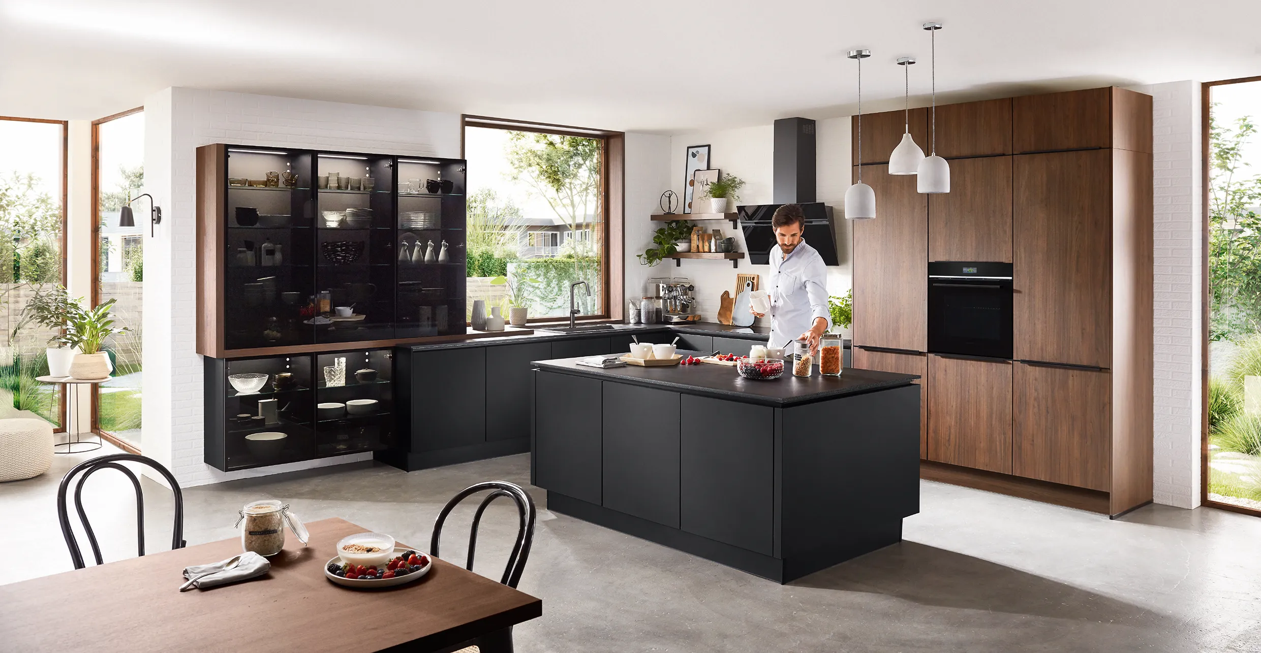 Contemporary kitchen with dark cabinets, natural wood panelled walls, and open shelving, featuring a man preparing a meal at the island. Contemporary kitchen with dark cabinets, natural wood panelled walls, and open shelving, featuring a man preparing a meal at the island.