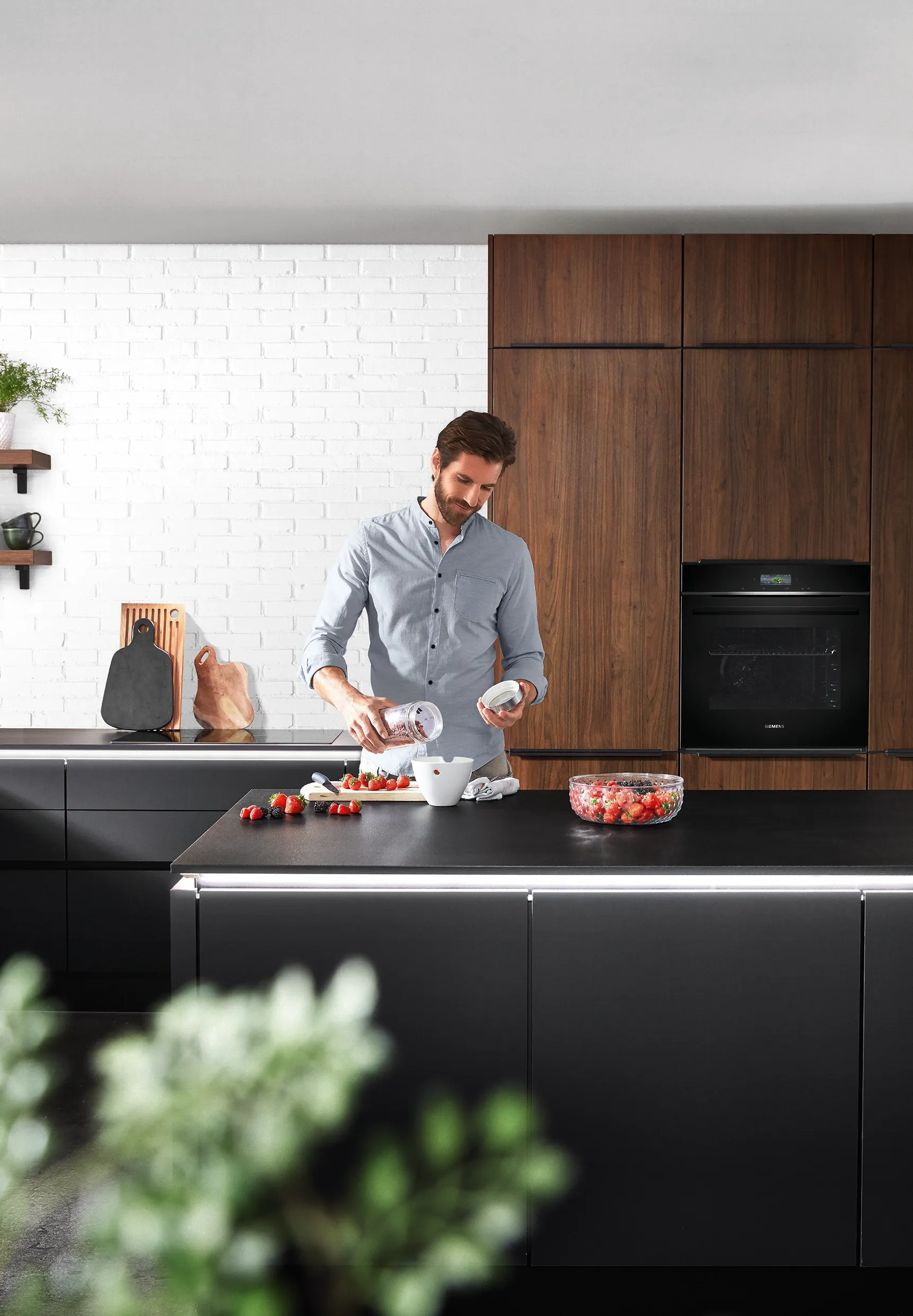 Man preparing food in a minimalist kitchen with dark cabinetry and wood accents, showcasing a sleek, modern design with an uncluttered aesthetic. Man preparing food in a minimalist kitchen with dark cabinetry and wood accents, showcasing a sleek, modern design with an uncluttered aesthetic.