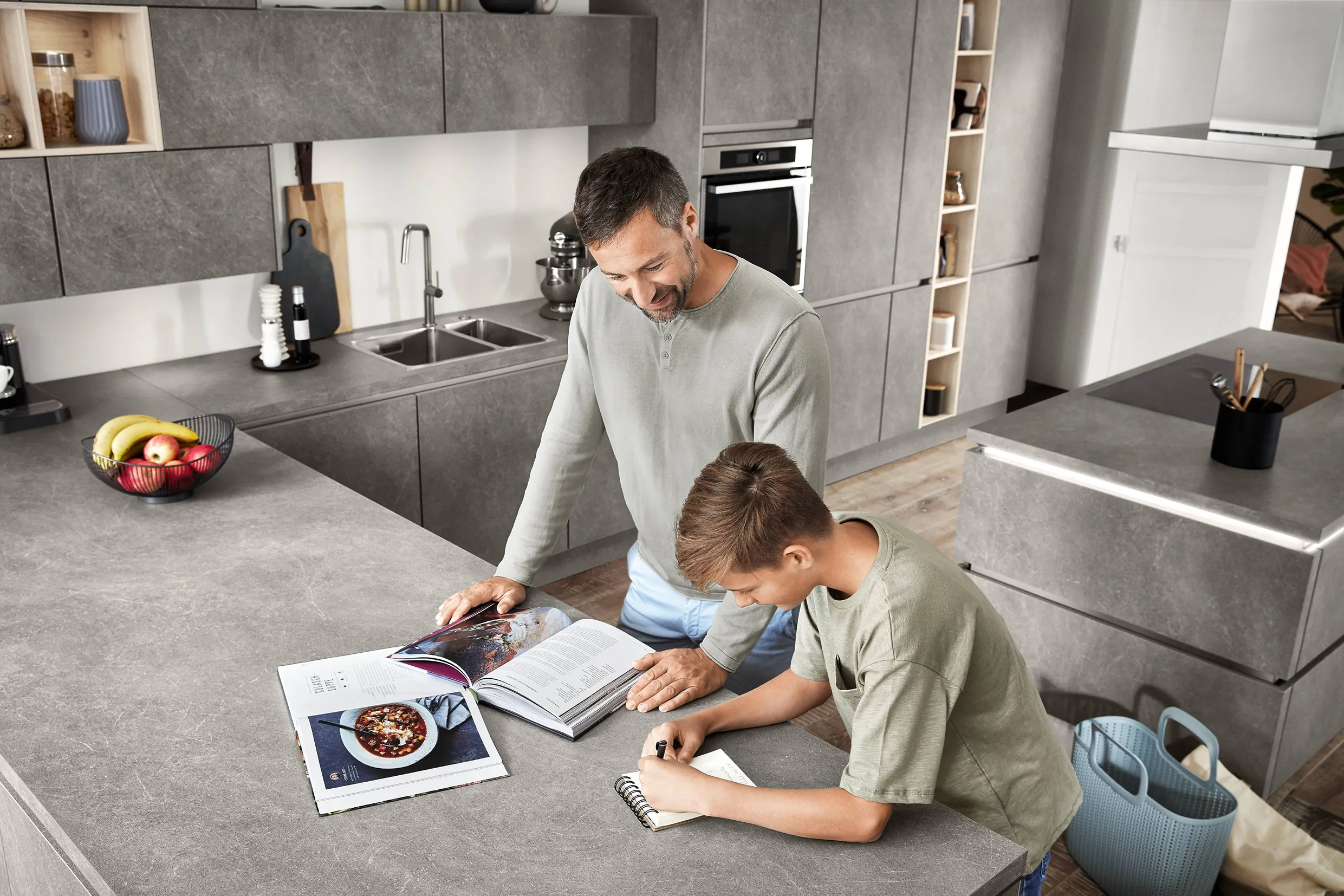 Modern grey kitchen with stone-effect cabinets, showcasing a father and son bonding while working on a project at the island counter. Modern grey kitchen with stone-effect cabinets, showcasing a father and son bonding while working on a project at the island counter.