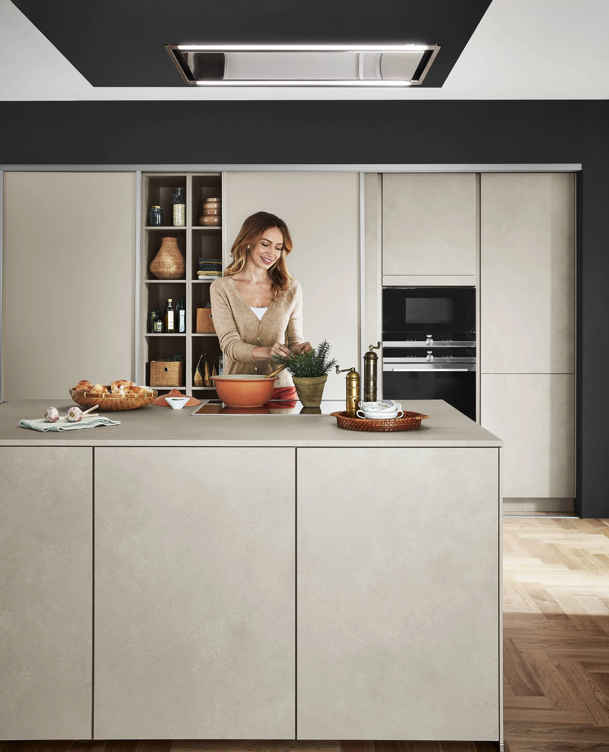 Modern beige kitchen with a sleek island, built-in shelving, and a woman preparing herbs, creating a warm and cohesive design aesthetic. Modern beige kitchen with a sleek island, built-in shelving, and a woman preparing herbs, creating a warm and cohesive design aesthetic.