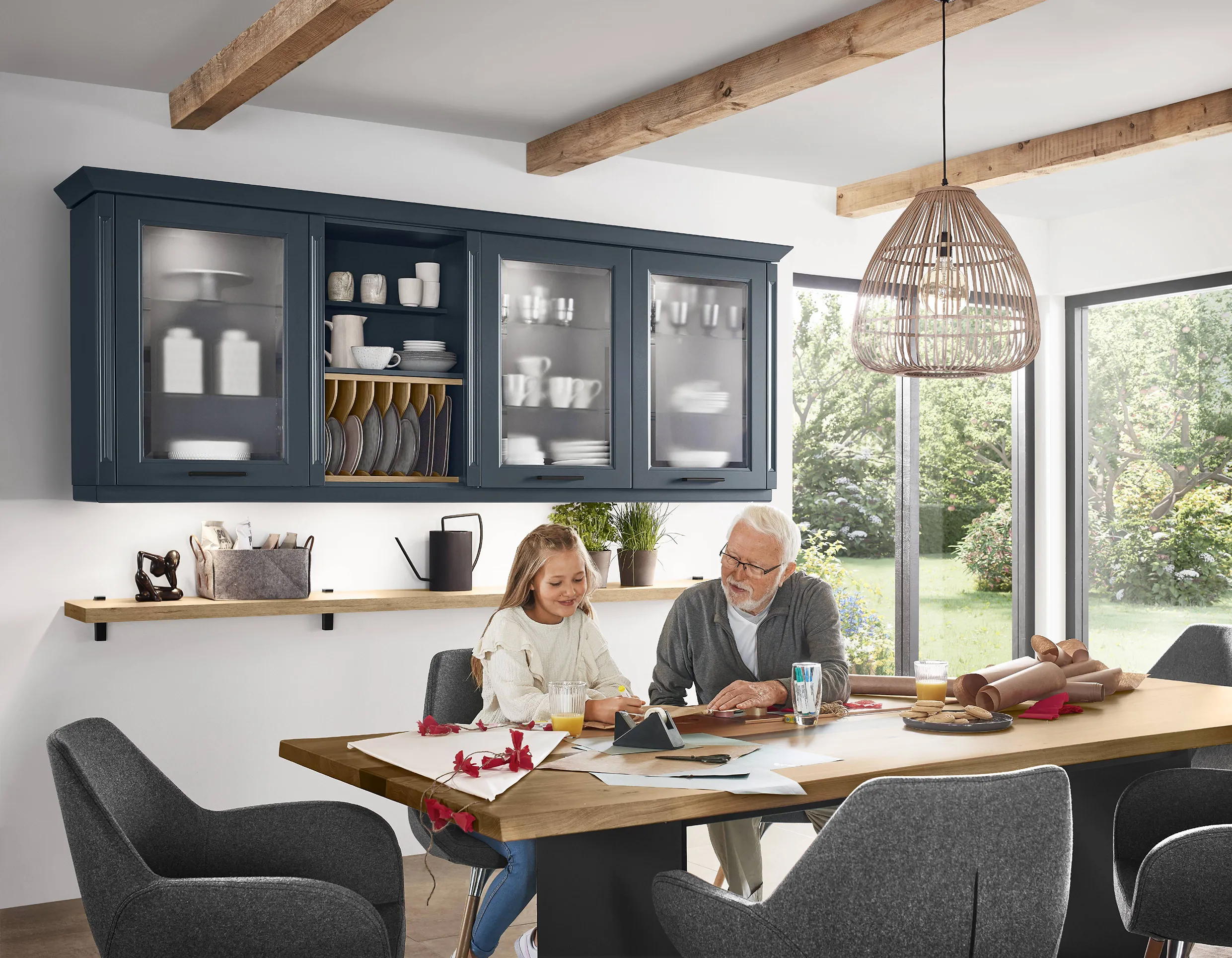 Modern kitchen with open shelving and dark blue cabinets, featuring a natural wood dining table where a grandfather and granddaughter enjoy a craft activity. Modern kitchen with open shelving and dark blue cabinets, featuring a natural wood dining table where a grandfather and granddaughter enjoy a craft activity.
