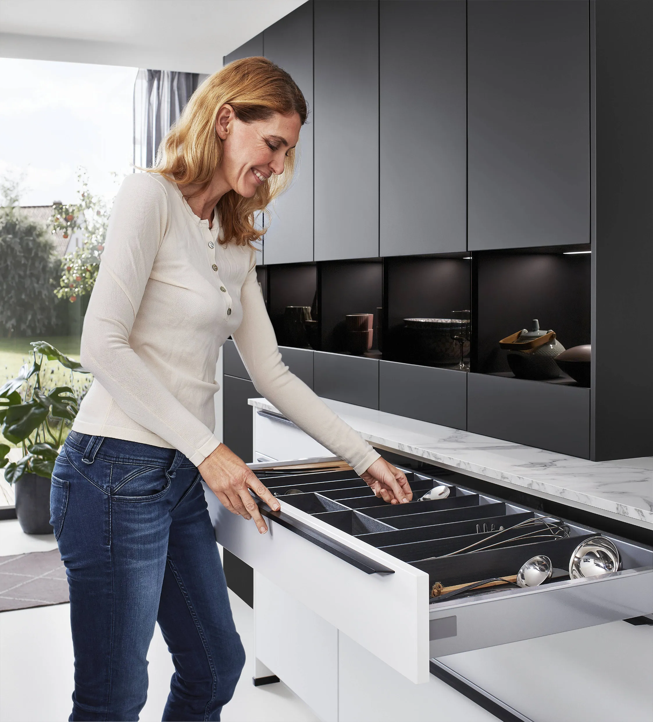 Woman organising utensils in a modern kitchen drawer with sleek black cabinets, highlighting minimalist cabinet hardware and functional design. Woman organising utensils in a modern kitchen drawer with sleek black cabinets, highlighting minimalist cabinet hardware and functional design.
