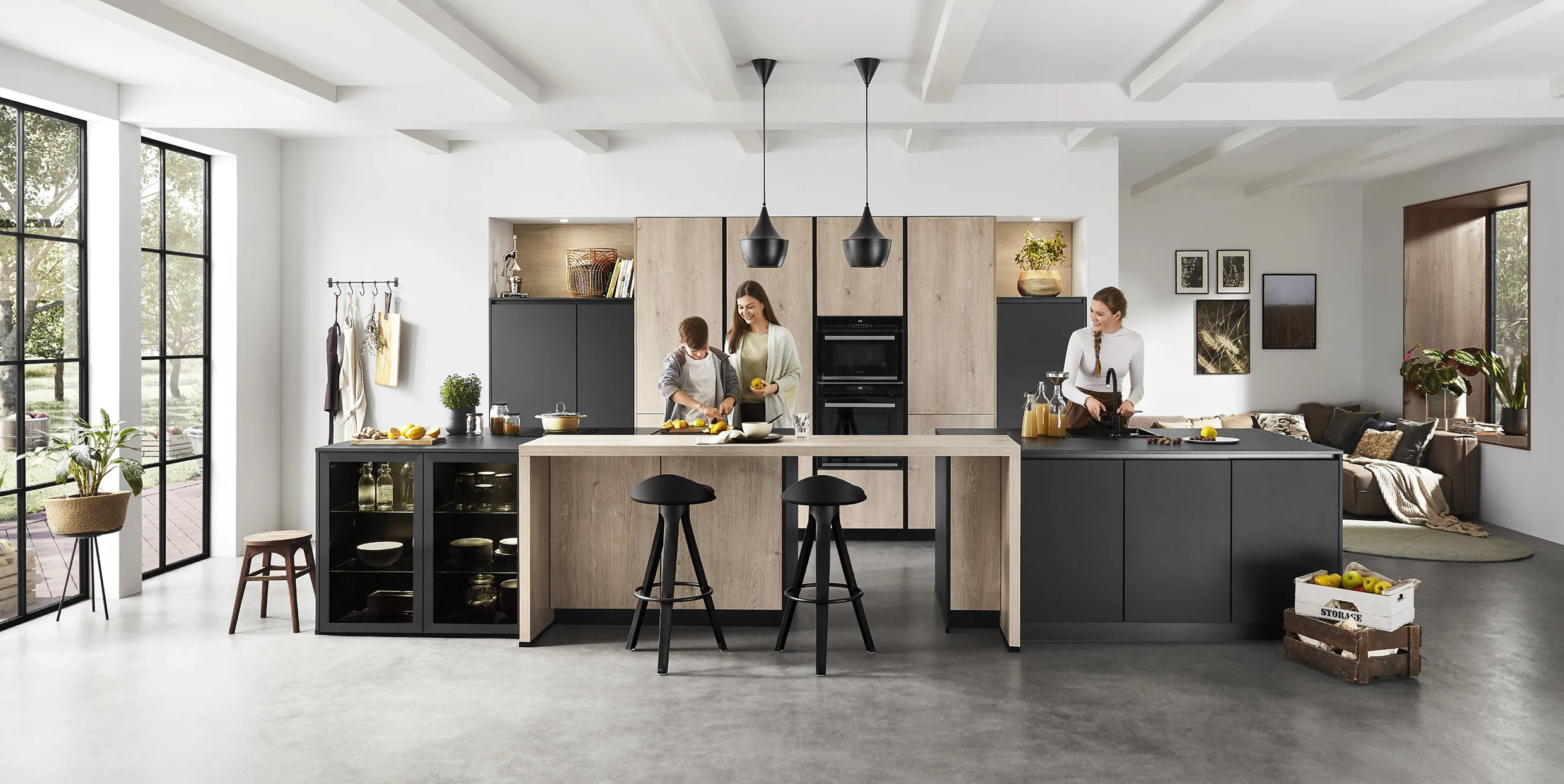 Family preparing food in a modern kitchen with light wood and black cabinets, featuring a large island, open seating, and natural light for social gatherings. Family preparing food in a modern kitchen with light wood and black cabinets, featuring a large island, open seating, and natural light for social gatherings.