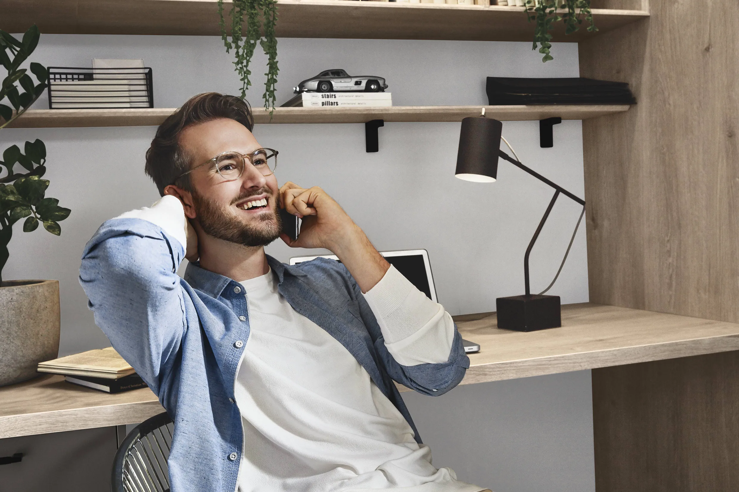 Man in a modern home office with natural wood shelving, plants, and a well-organised desk, illustrating a blend of style and technology. Man in a modern home office with natural wood shelving, plants, and a well-organised desk, illustrating a blend of style and technology.
