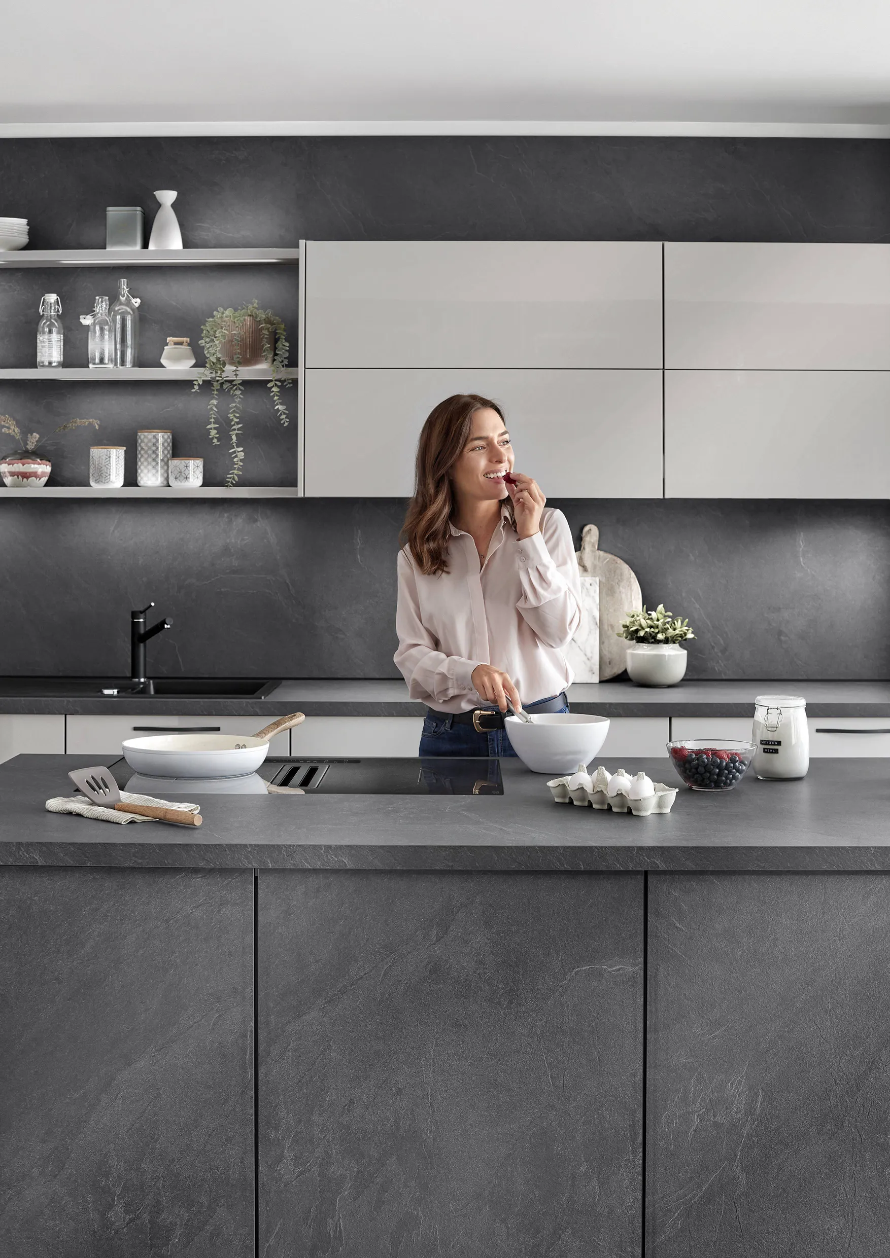 Woman enjoying a snack in a two-tone kitchen with grey and white cabinets, showcasing modern design and smooth countertops. Woman enjoying a snack in a two-tone kitchen with grey and white cabinets, showcasing modern design and smooth countertops.