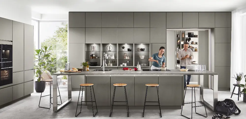 A man leaves the pantry storage of a modern kitchen while a woman is cooking A man leaves the pantry storage of a modern kitchen while a woman is cooking